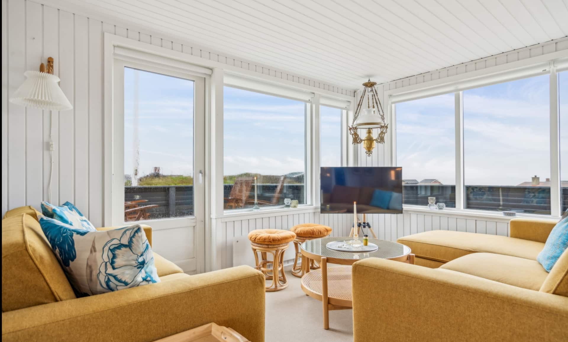 Lys stue med gule sofaer og vinduer mod klitterne